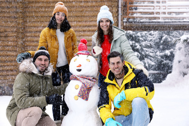 Photo of Happy friends with snowman outdoors on snowy day. Winter vacation