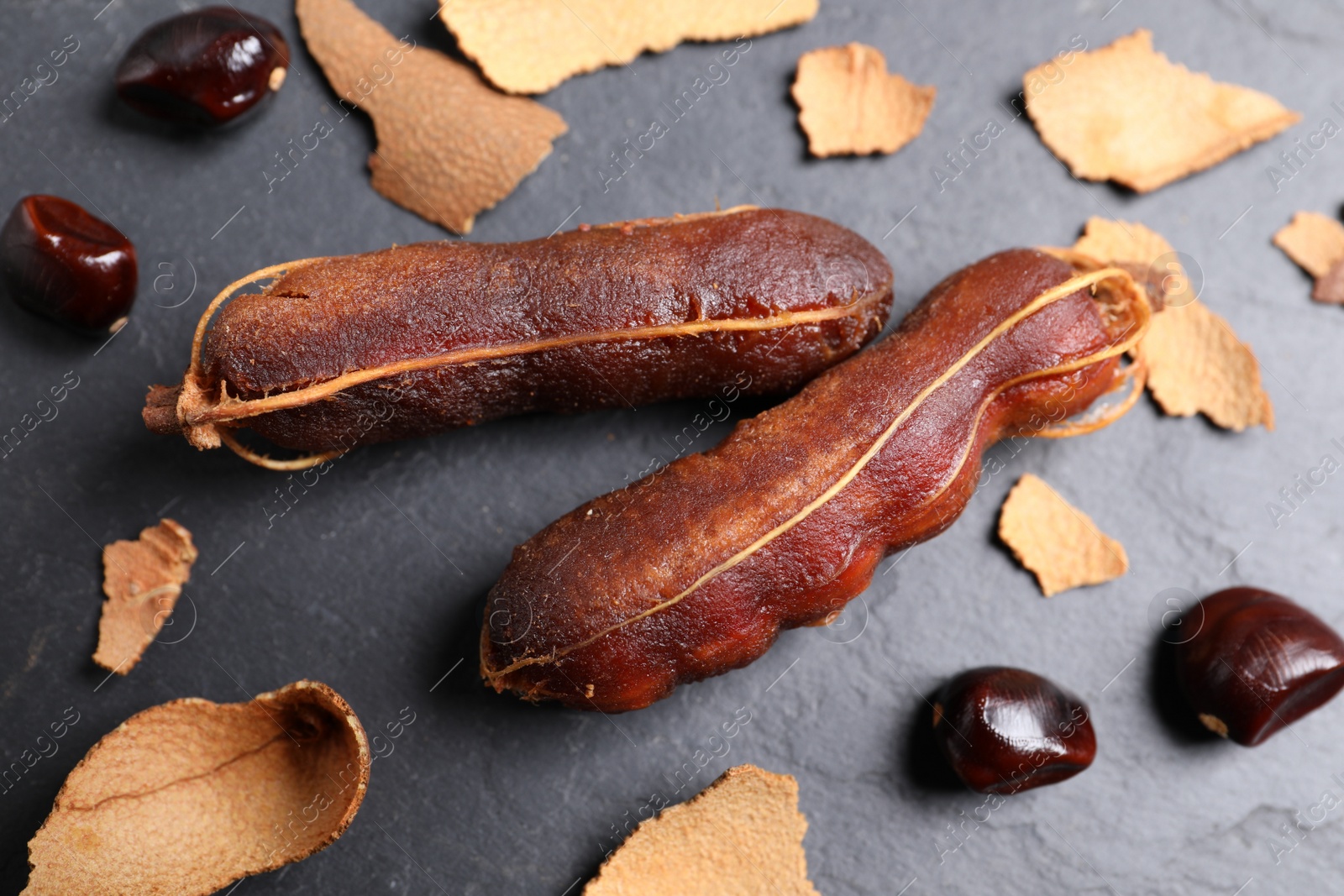 Photo of Peeled tamarind pods and seeds on black table, flat lay