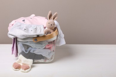 Laundry basket with baby clothes on white wooden table, space for text