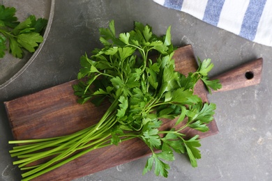 Wooden board with fresh green parsley on grey background, top view