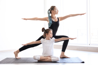 Photo of Little girl and her teacher practicing yoga in gym
