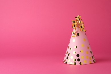 Photo of One beautiful party hat with serpentine streamers on pink background. Space for text