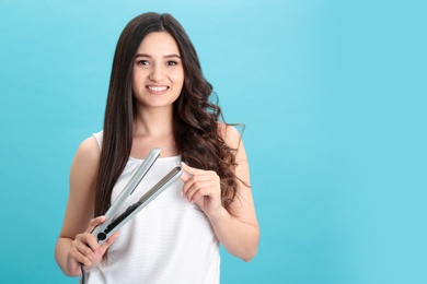 Photo of Young woman with modern hair iron on blue background, space for text