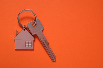 Photo of Metallic key with keychain in shape of house on orange background, top view. Space for text