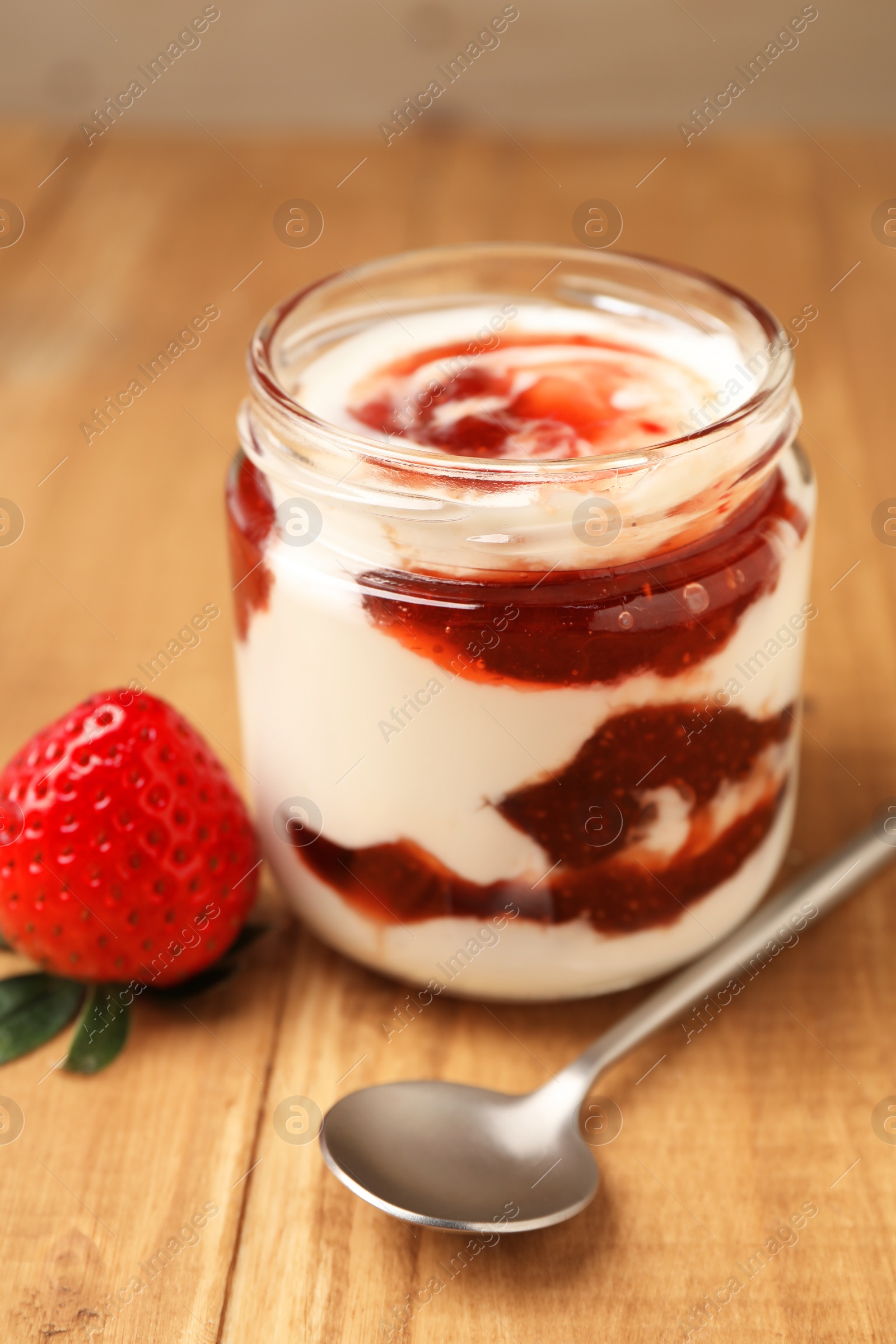 Photo of Tasty yoghurt with jam, spoon and strawberry on wooden table, closeup