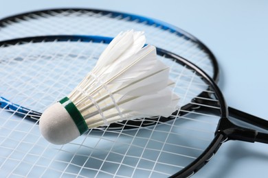 Feather badminton shuttlecock and rackets on light blue background, closeup