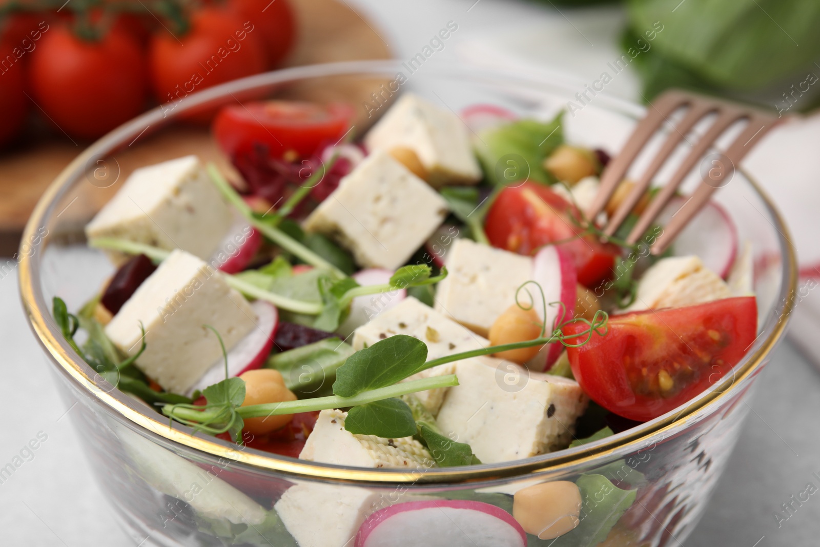 Photo of Bowl of tasty salad with tofu and vegetables on light grey table, closeup