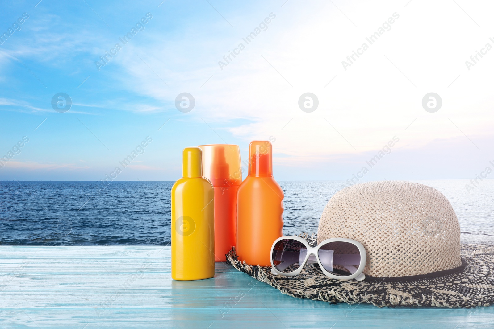 Image of Set of sun protection products and stylish accessories on wooden table near sea