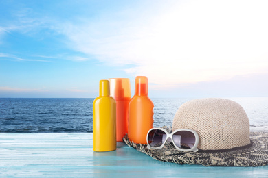 Image of Set of sun protection products and stylish accessories on wooden table near sea