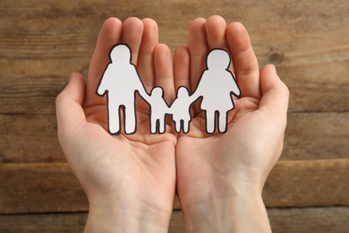 Photo of Woman holding paper family cutout on wooden background, closeup