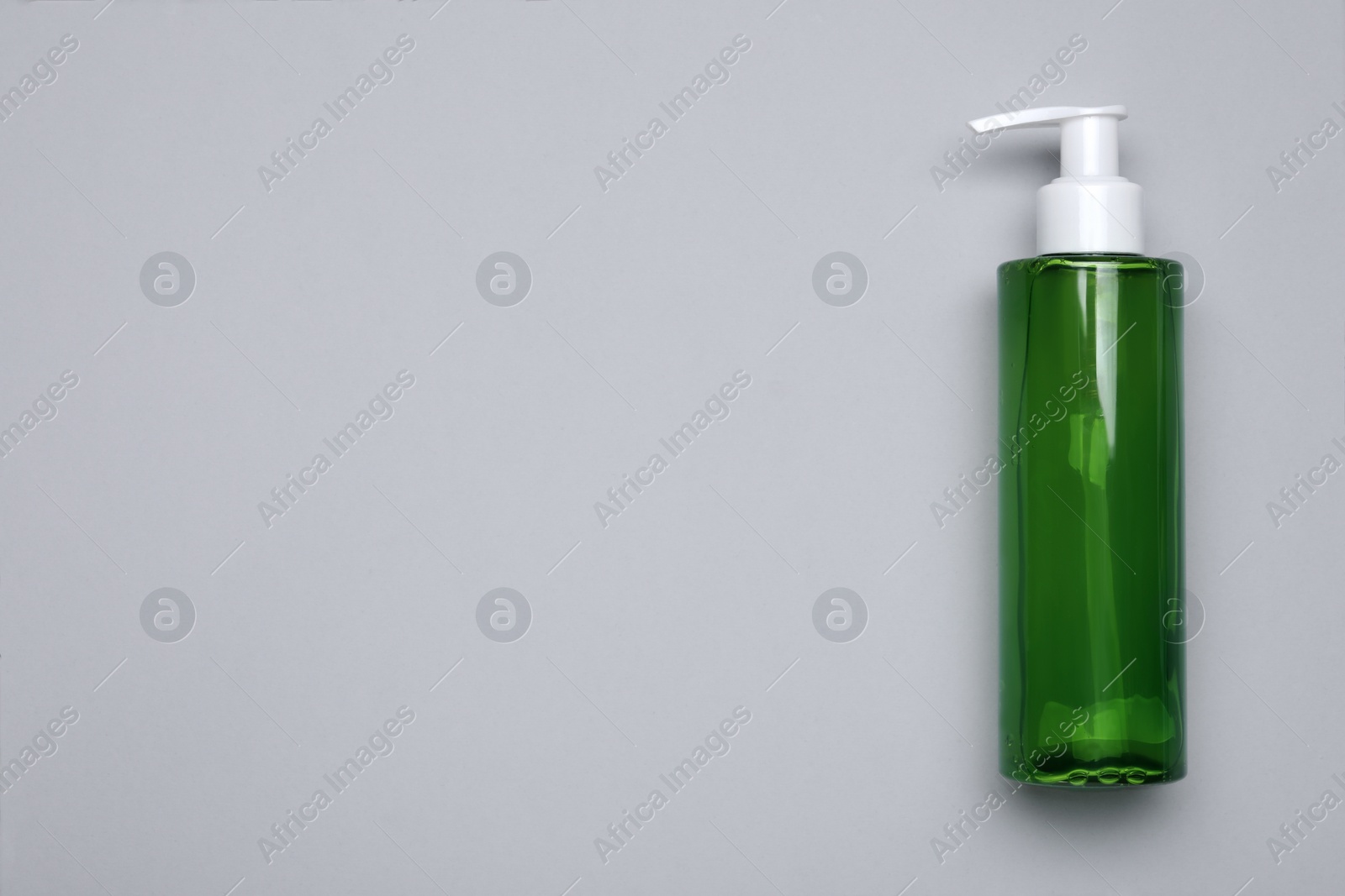 Photo of Bottle of face cleansing product on light grey background, top view. Space for text