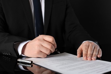 Photo of Notary signing document at black table, closeup