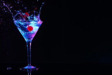 Photo of Adding cherries into glass with martini on black background, space for text