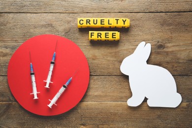 Photo of Cubes with text Cruelty Free, syringes and figure of rabbit on wooden table, flat lay. Stop animal tests