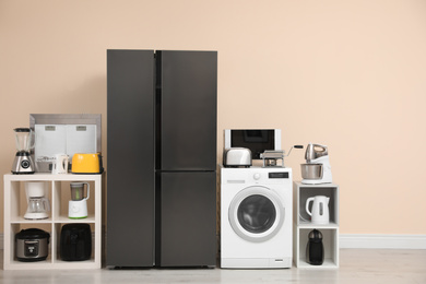 Photo of Modern refrigerator and other household appliances near beige wall indoors