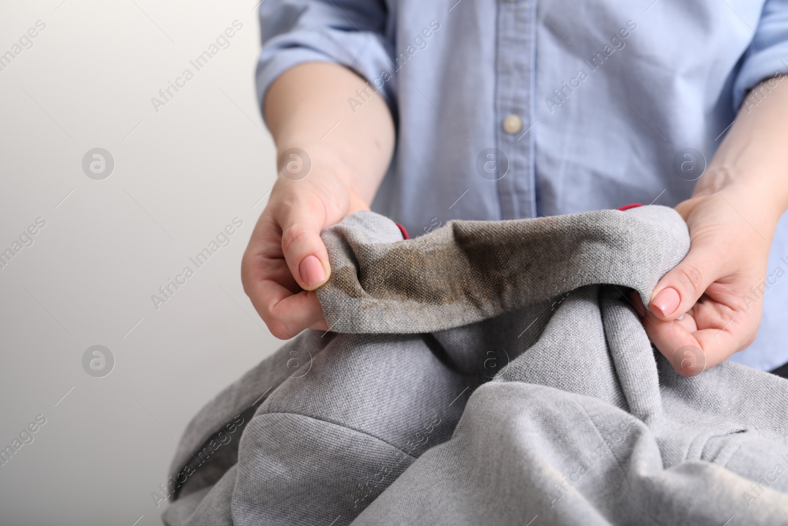 Photo of Woman showing stain from coffee on jacket against light grey background, closeup