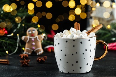 Delicious hot chocolate with marshmallows and cinnamon near Christmas decor on black table against blurred lights, space for text