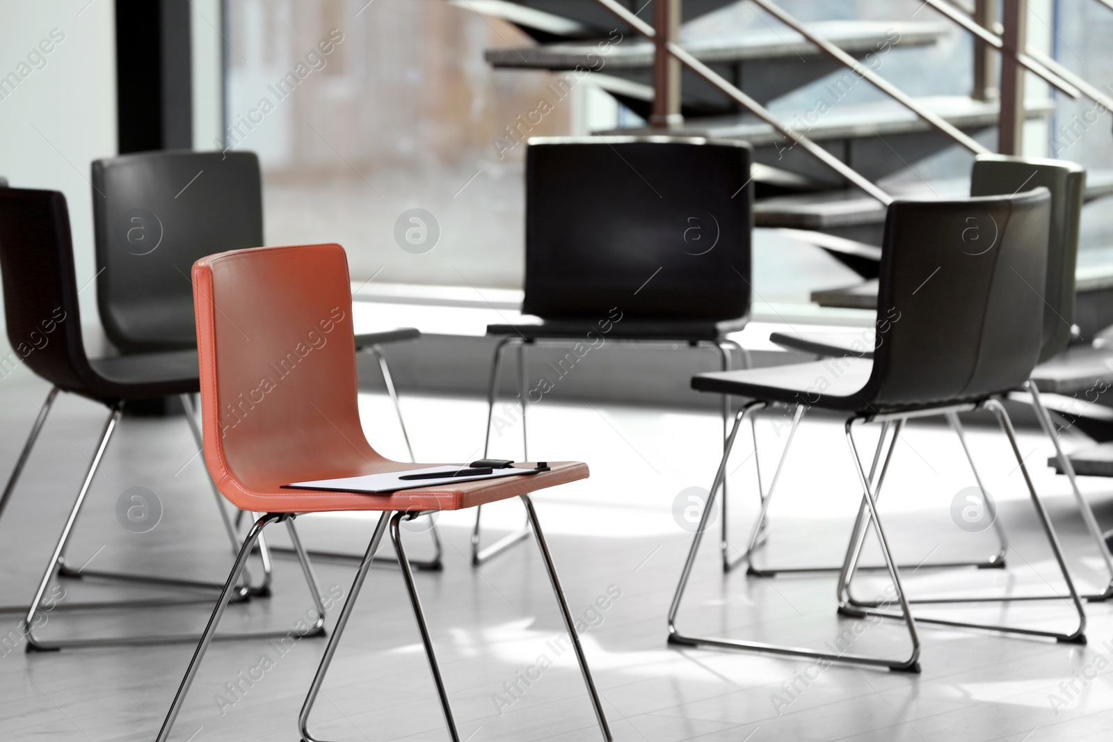 Photo of Red chair with clipboard in office prepared for group therapy. Meeting room interior