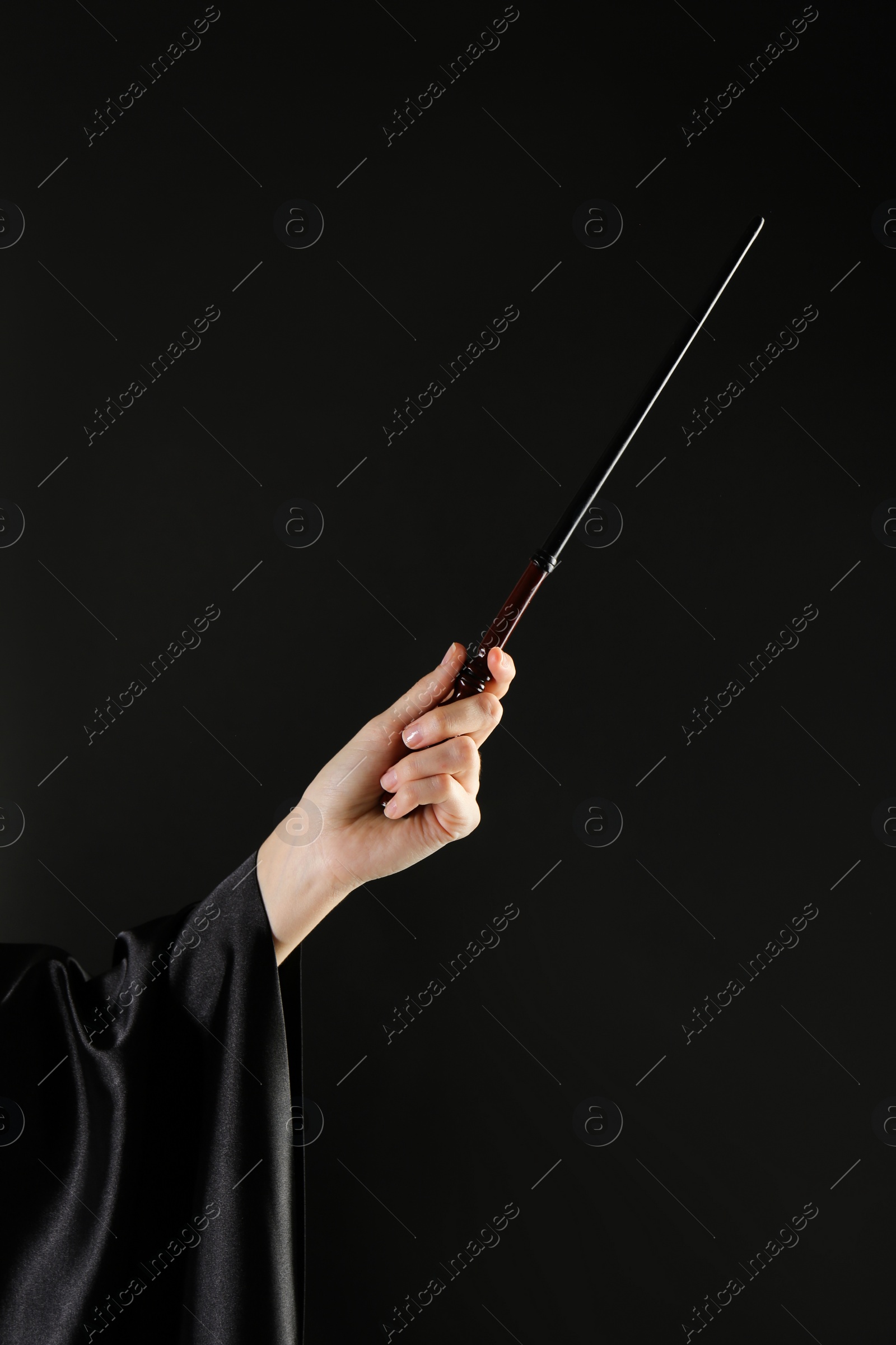 Photo of Wizard holding magic wand on black background, closeup