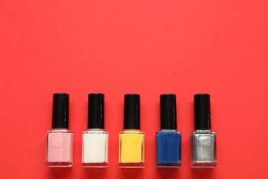 Bright nail polishes in bottles on red background, flat lay. Space for text