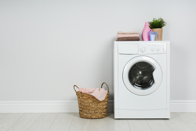 Photo of Modern washing machine with stack of towels, detergents and laundry basket near white wall. Space for text