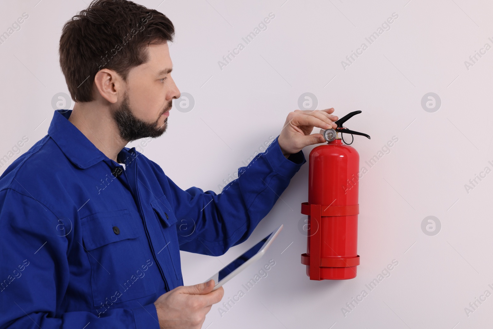 Photo of Man with tablet checking fire extinguisher indoors