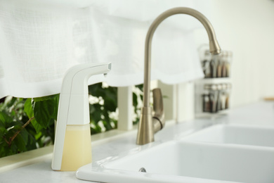 Photo of Modern automatic soap dispenser near sink in kitchen
