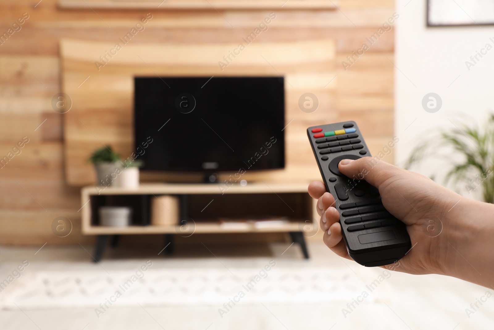 Photo of Young man switching channels on TV set with remote control at home, closeup