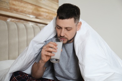 Photo of Man taking medicine for hangover in bedroom at home