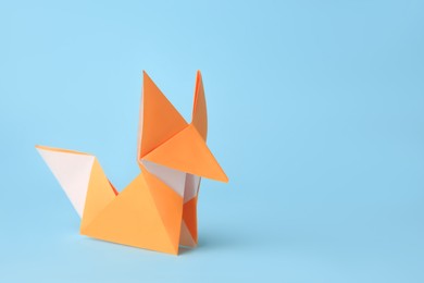 Photo of Origami art. Handmade orange paper fox on light blue background, space for text