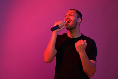 Photo of Handsome man with microphone singing on pink background, space for text. Color tone effect