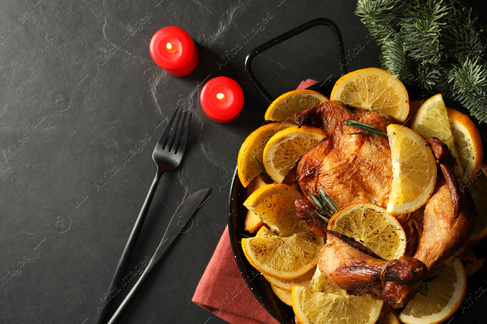 Photo of Baked chicken with orange slices and burning candles on black table, flat lay