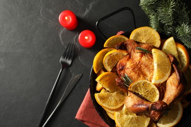 Photo of Baked chicken with orange slices and burning candles on black table, flat lay