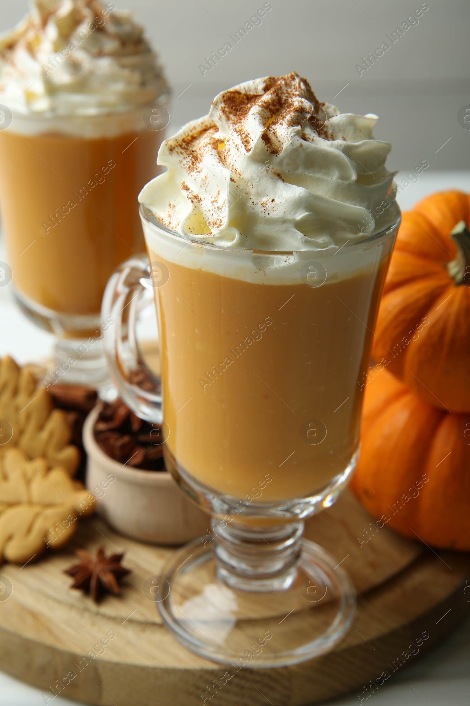 Photo of Tasty pumpkin latte with whipped cream in glasses, spices and cookies on white table, closeup