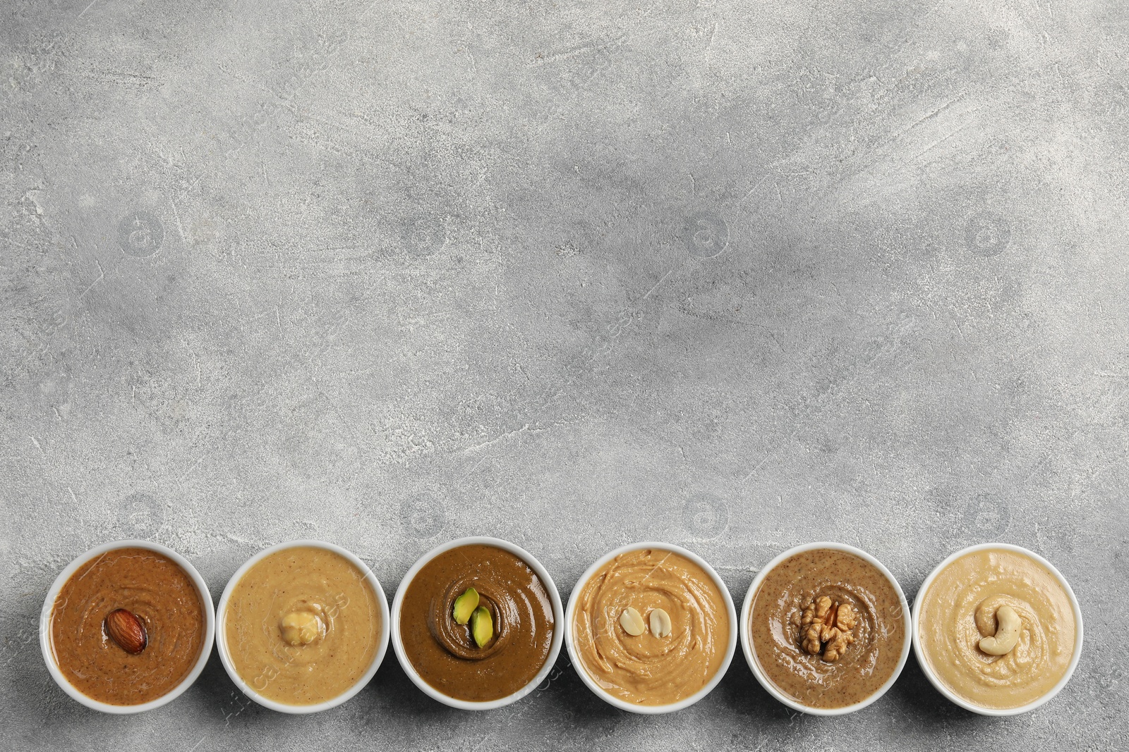 Photo of Tasty nut butters in bowls on light grey background, flat lay. Space for text