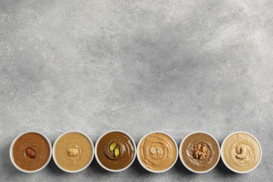 Tasty nut butters in bowls on light grey background, flat lay. Space for text