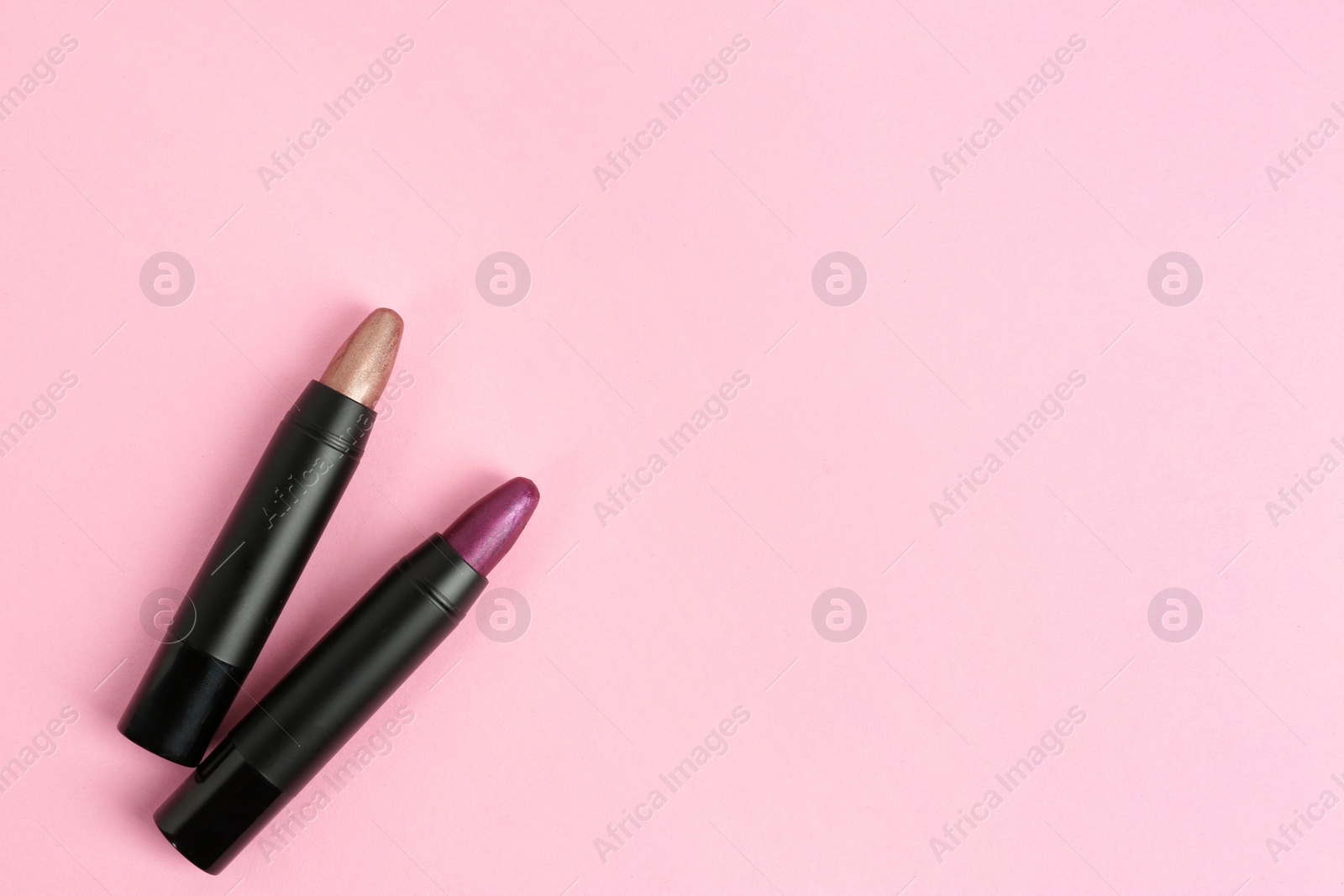 Photo of Bright lipsticks in black tubes on pink background, flat lay. Space for text