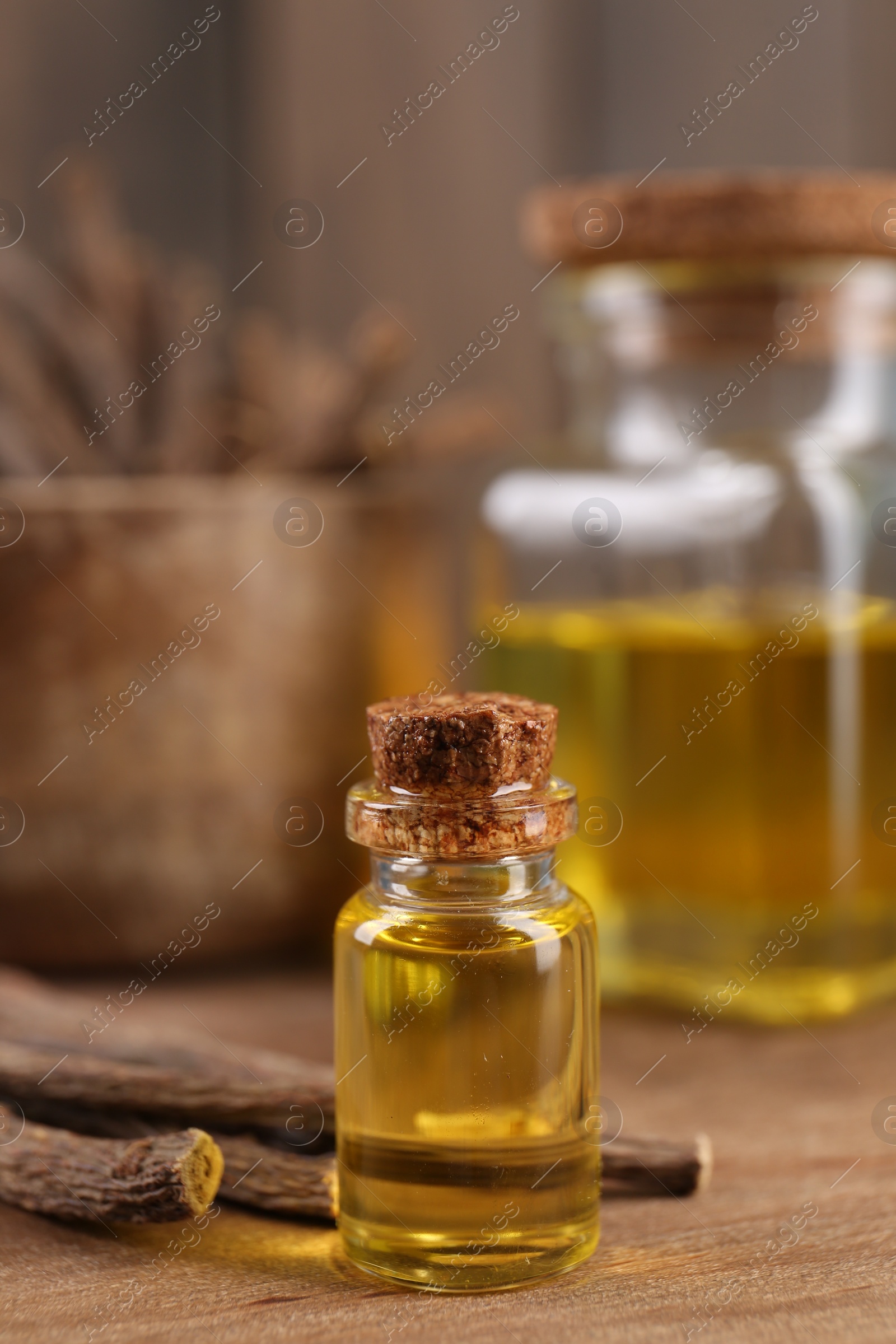 Photo of Dried sticks of licorice roots and essential oil on wooden board, closeup