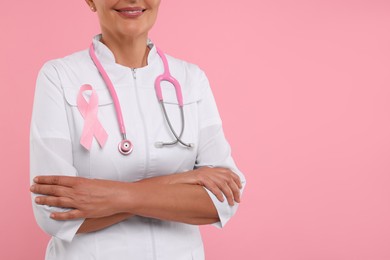 Photo of Doctor with pink ribbon and stethoscope on color background, closeup and space for text. Breast cancer awareness