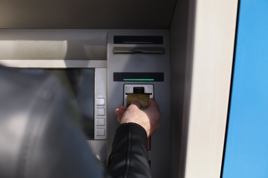 Photo of Man inserting credit card into cash machine outdoors, closeup