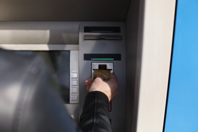 Man inserting credit card into cash machine outdoors, closeup