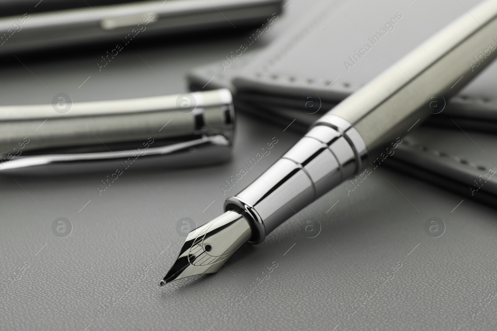 Photo of Stylish silver fountain pen on grey textured table, closeup
