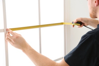 Photo of Service man measuring window for installation indoors, closeup