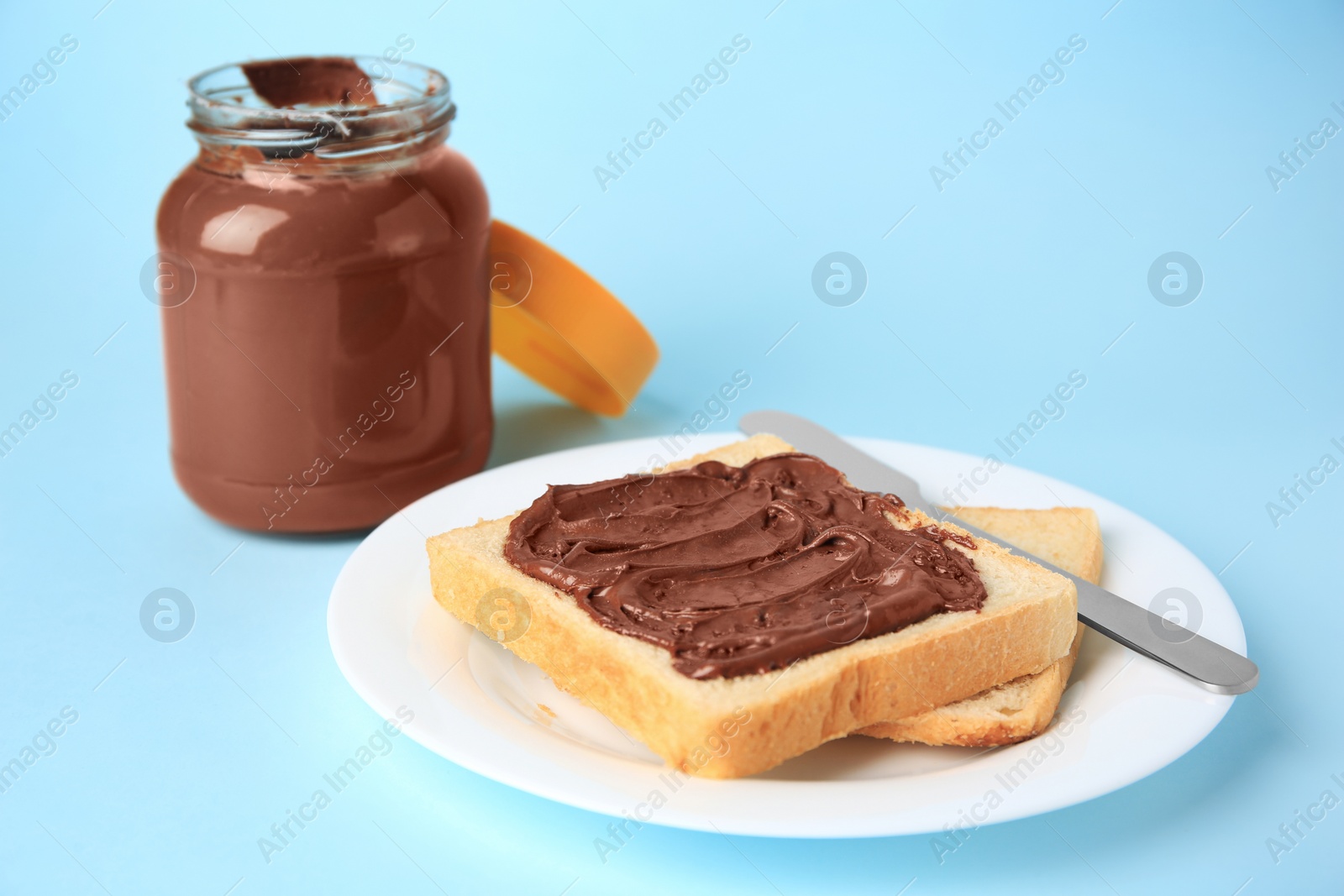 Photo of Tasty toast with chocolate paste and jar of cream on light blue background