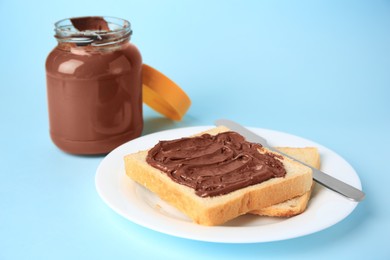 Tasty toast with chocolate paste and jar of cream on light blue background