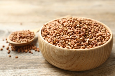 Photo of Bowl of uncooked buckwheat on wooden table