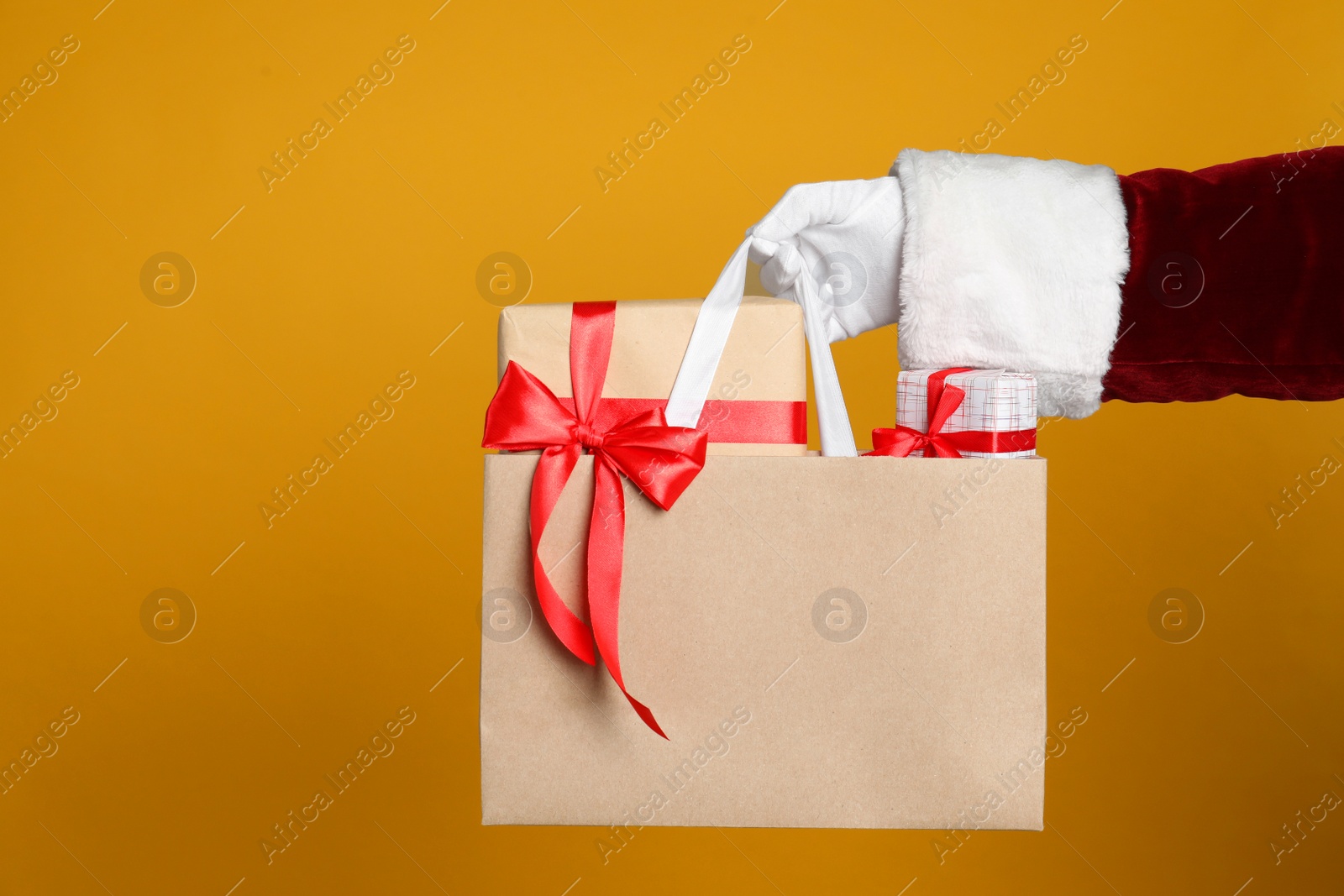 Photo of Santa holding paper bag with gift boxes on orange background, closeup