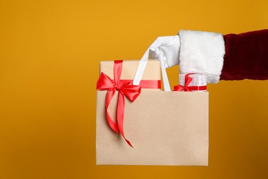 Photo of Santa holding paper bag with gift boxes on orange background, closeup