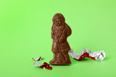 Photo of Sweet chocolate Santa Claus candy and pieces of foil wrapper on light green background