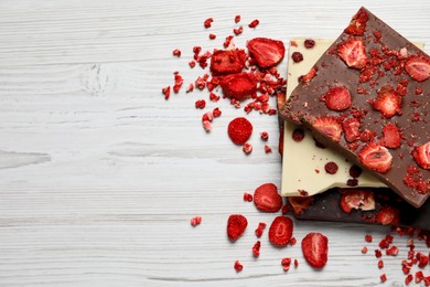 Photo of Different chocolate bars with freeze dried fruits on white wooden table, flat lay. Space for text